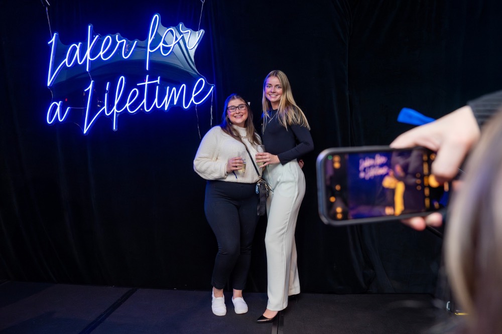 Two girls wearing black and white pose in front of Lakers for a Lifetime neon sign while someone takes their picture